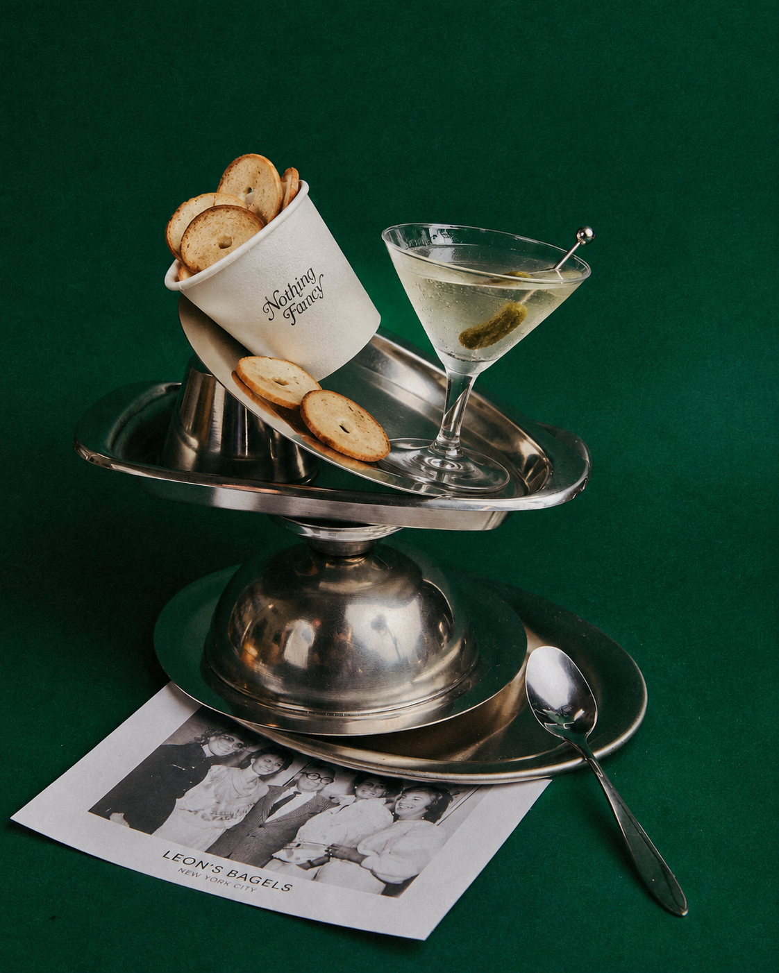 A martini and bagel chips on a silver tray against a deep green background