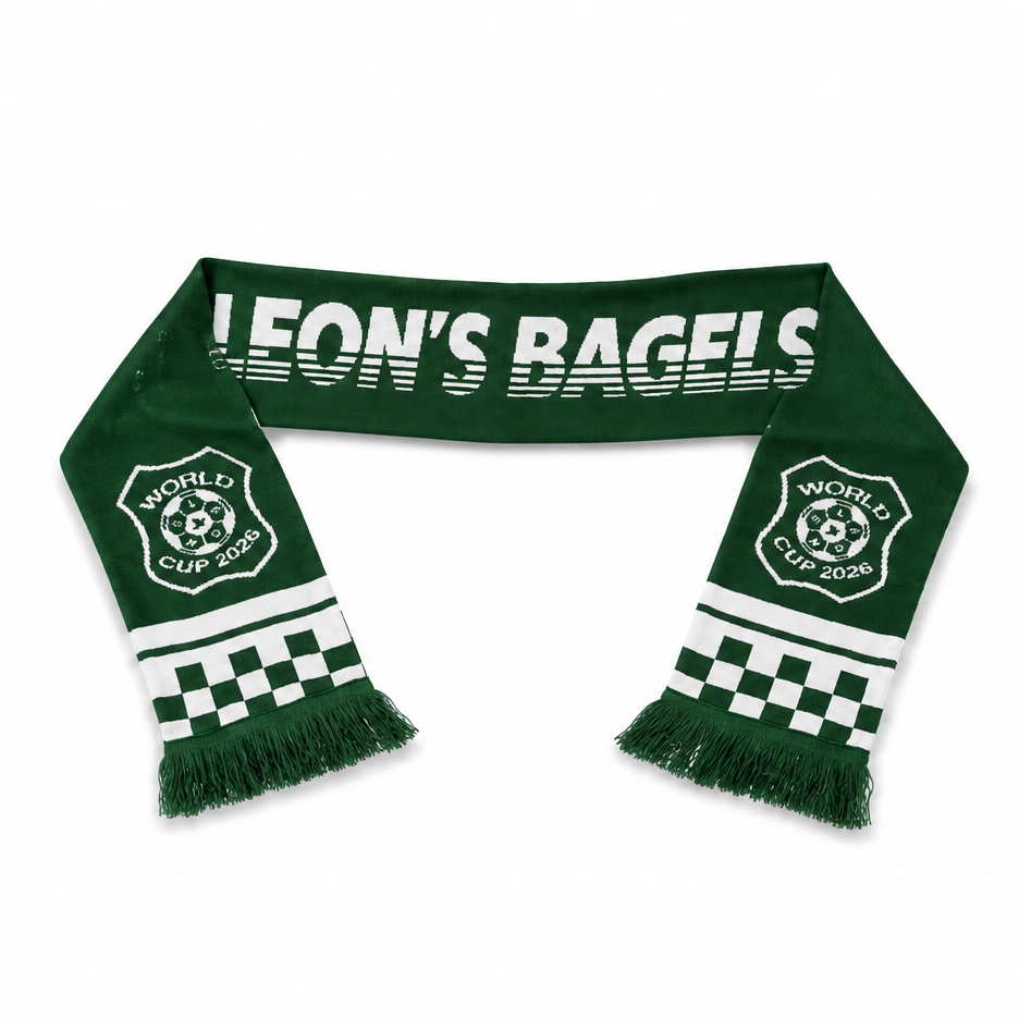 A green and white knit scarf featuring the text 'LEON'S BAGELS' and 'WORLD CUP CUP 2025' with a soccer ball emblem, checkered patterns, and fringed ends, displayed on a white background.