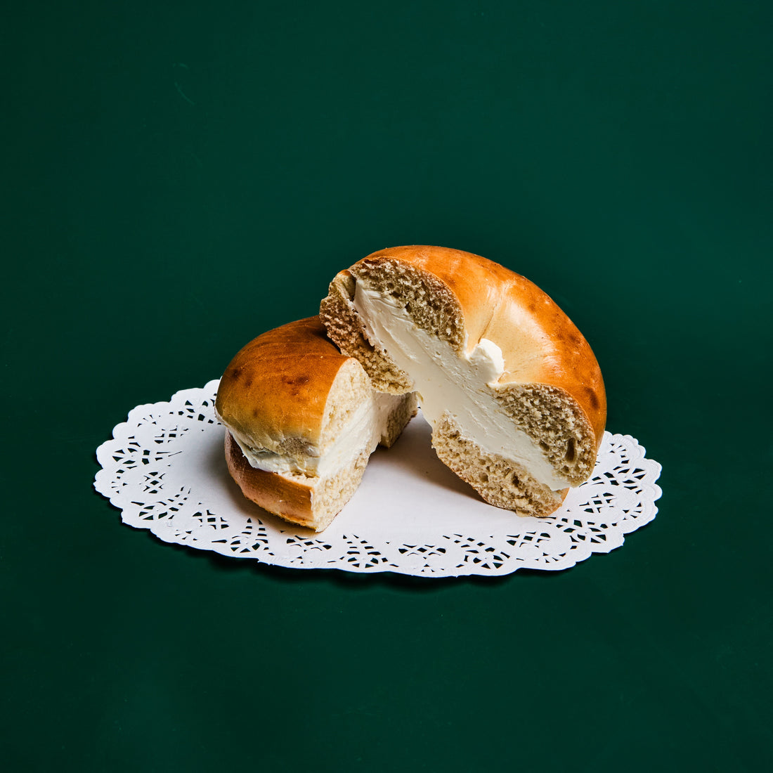 A plain bagel split and filled with cream cheese, on a paper doily