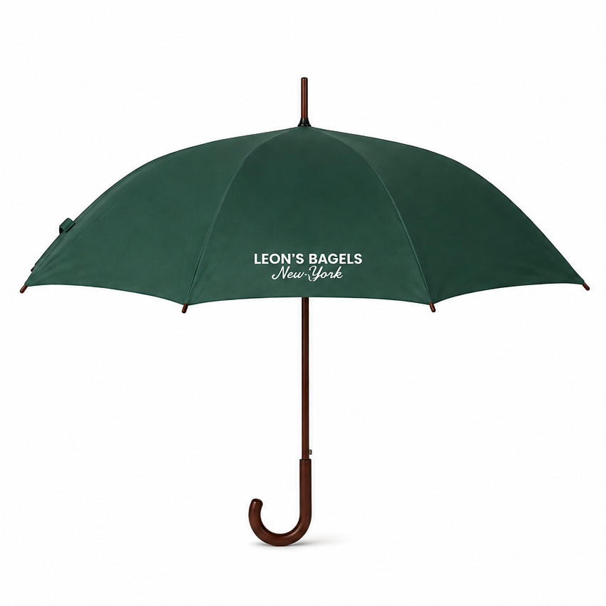 A dark green open umbrella with a brown wooden handle and shaft, featuring the white printed text 'LEON'S BAGELS New York' on the canopy, set against a plain white background.