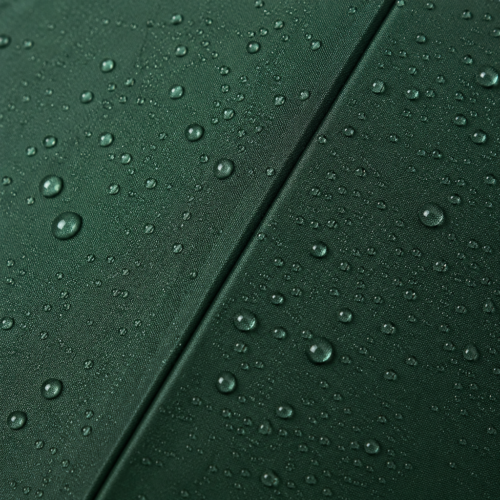 Close-up of a dark green fabric surface with water droplets beaded across it and a diagonal seam running through the center.