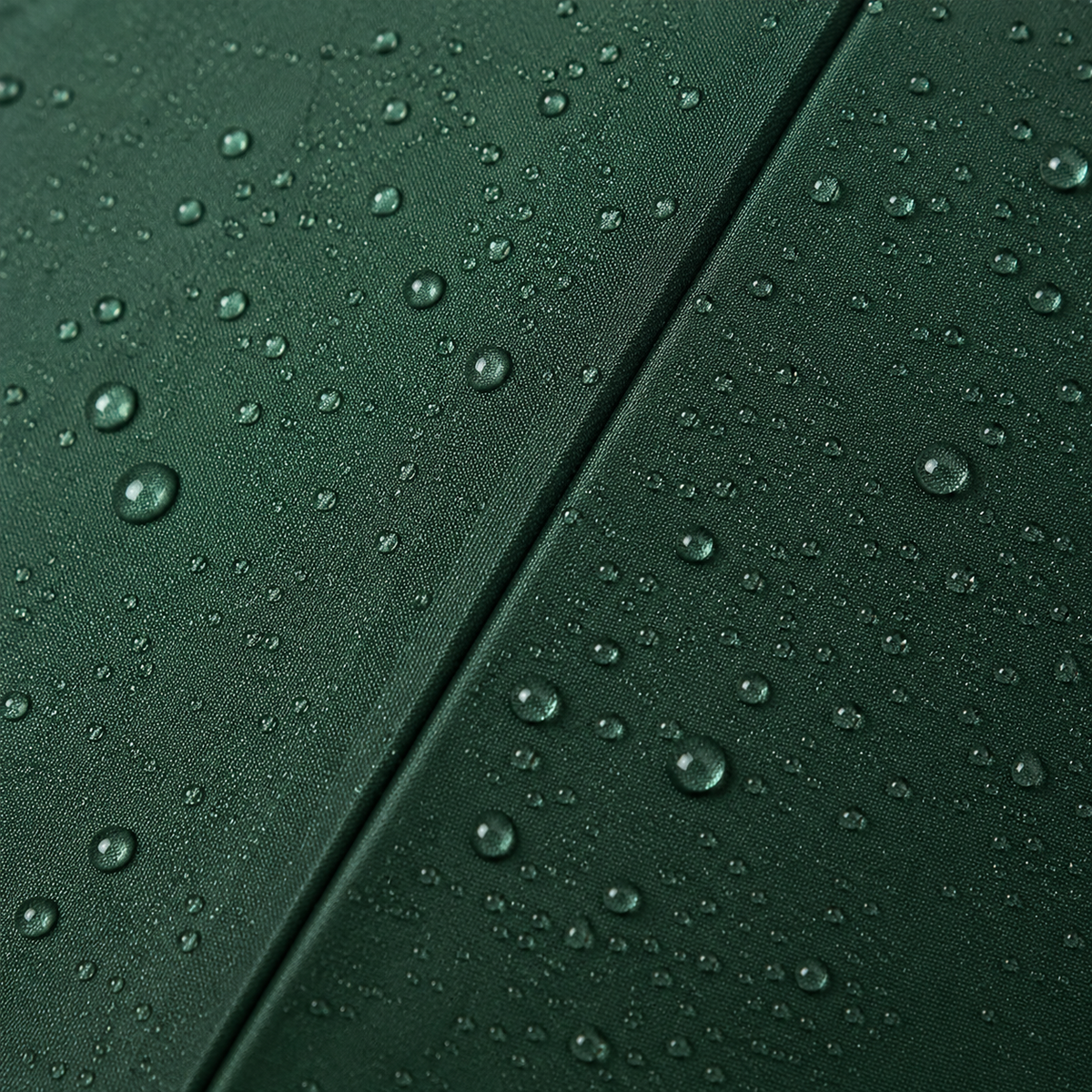 Close-up of a dark green fabric surface with water droplets beaded across it and a diagonal seam running through the center.